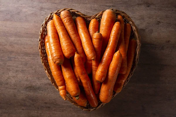 Wiele marchewki pęczek w koszyku serca na drewnianym tle — Zdjęcie stockowe