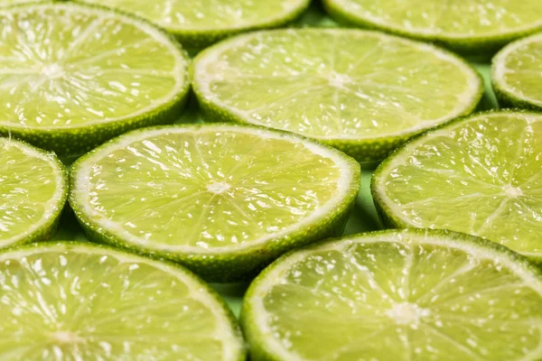 Een plakjes verse sappige groene citroenen. groene achtergrond, patroon. — Stockfoto