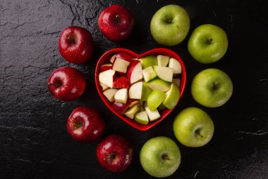 Olgun kırmızı ve yeşil elma masayakın üzerinde kalp kase içine.