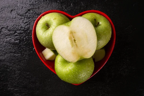 Ripe green apples into heart bowl on table close up