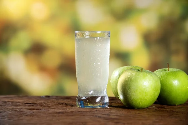 Frutta e succo di mela verde in un bicchiere su un tavolo di legno, all'aperto — Foto Stock