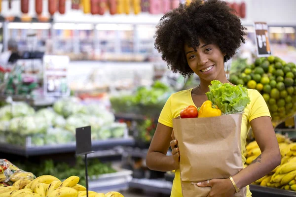 Friska positiva lycklig afrikansk kvinna som innehar en papperspåse full av frukt och grönsaker. — Stockfoto