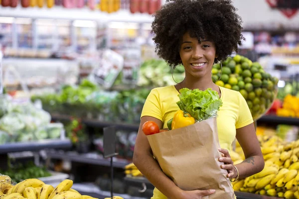 Friska positiva lycklig afrikansk kvinna som innehar en papperspåse full av frukt och grönsaker. — Stockfoto