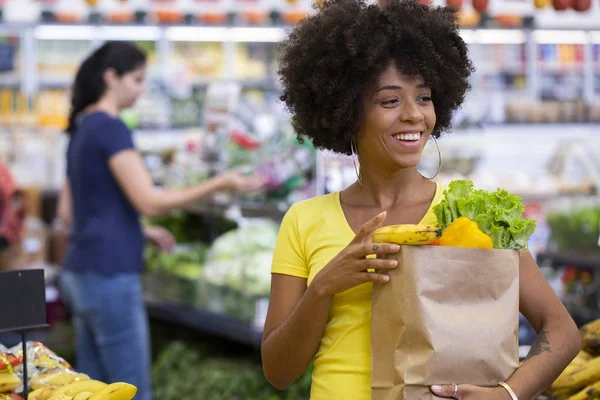 Friska positiva lycklig afrikansk kvinna som innehar en papperspåse full av frukt och grönsaker. — Stockfoto