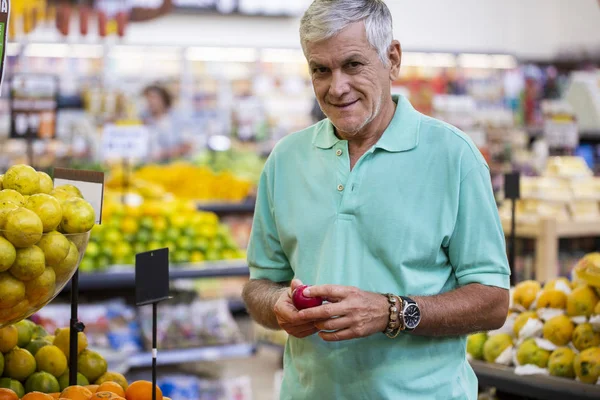 Stilig man poserar, tittar på kameran och håller melon i handen. Skäggiga kund leende. Avsnitt med färska citrus på bakgrund. — Stockfoto