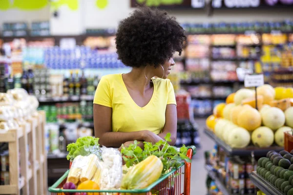 Saludable positiva mujer africana feliz sosteniendo un carrito de compras lleno de frutas y verduras —  Fotos de Stock