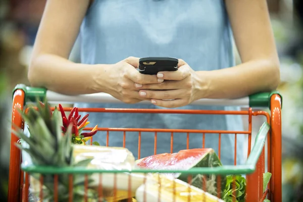 Kvinna som använder mobiltelefon när du handlar i snabbköpet — Stockfoto