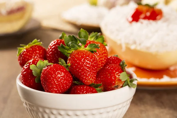 Diverse fragole in una pentola bianca su un tavolo di legno — Foto Stock