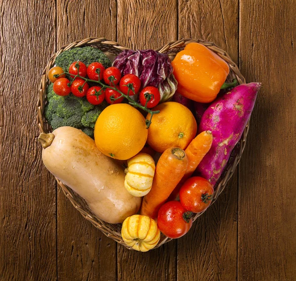 Basket in heart shape filled with fruits and vegetables on an old wooden background, top view