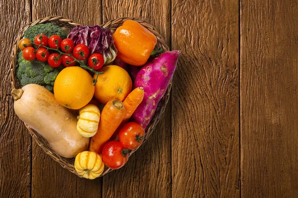 Eski ahşap arka plan üzerinde meyve ve sebzelerle dolu kalp şeklinde sepet, metin için alan ile üst görünüm