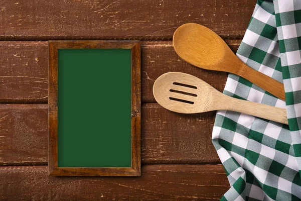 Restaurant menu. Top view of chalkboard menu laying on the rustic wooden desk with spoons and green napkin.Top view