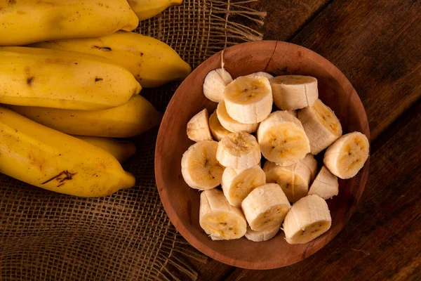 A banch of bananas and a sliced banana on wood background