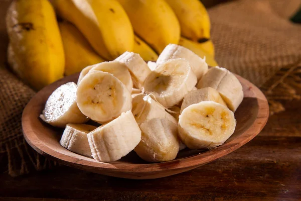 A banch of bananas and a sliced banana on wood background
