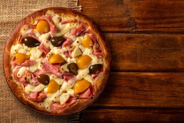 Sweet pizza with peaches, fig and pineapple on wood background. Top view, close up. Traditional Brazilian Pizza