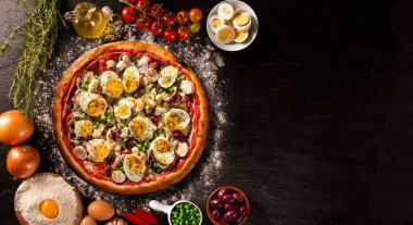 Geleneksel Portekiz pizzası, yumurta, zeytin, palmiye kalbi ve bezelye. Siyah beton arka plan üst görünümü, yakın çekim. Geleneksel Brezilya Pizzası