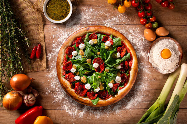 Brazilian pizza with dried tomato, arugula and mustard. Top view on wood background, close up. Traditional Brazilian Pizza.