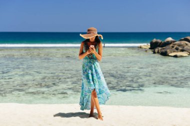 tropik plajda Smartphone tutan mutlu kadın. Erkek seyahat ve smartphone Seyşeller plaj üzerinde kullanın.