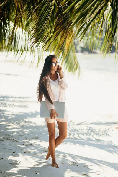 Woman freelancer on the beach. Working remotely on the laptop computer through the internet. Working while travelling. Summer vacation in Seychelles.