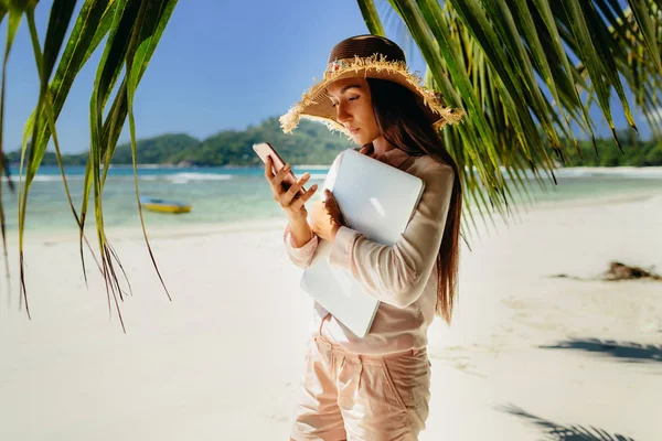 在海滩上用笔记本电脑打电话的女人 旅行时远程工作 塞舌尔暑假 — 图库照片