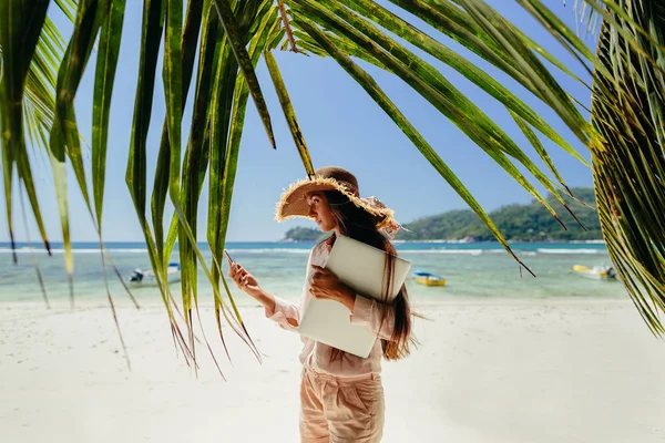 Sahilde dizüstü bilgisayar ile telefonda konuşurken bir kadın. Uzaktan seyahat ederken çalışma. Yaz tatili de Seyşeller.