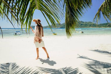 Sahilde kadın serbest meslek sahibi. Uzaktan internet üzerinden dizüstü bilgisayarda çalışma. Seyahat ederken çalışma. Yaz tatili de Seyşeller.