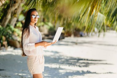 Sahilde dizüstü bilgisayarda uzaktan çalışan kadın. Seyahat ederken çalışmak. Seyşeller'de yaz tatili.