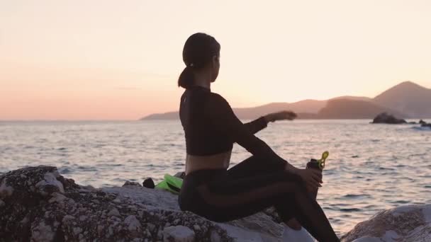 Sportif kadın sahilde rahatlar. Deniz manzaralı protein karıştırıcı içerler. — Stok video