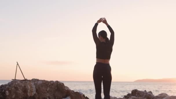 Donna sportiva in posa e che si estende sulla spiaggia al tramonto — Video Stock