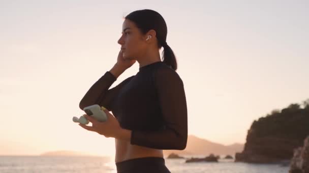 Mulher desportiva ouvir música na praia ao pôr do sol — Vídeo de Stock