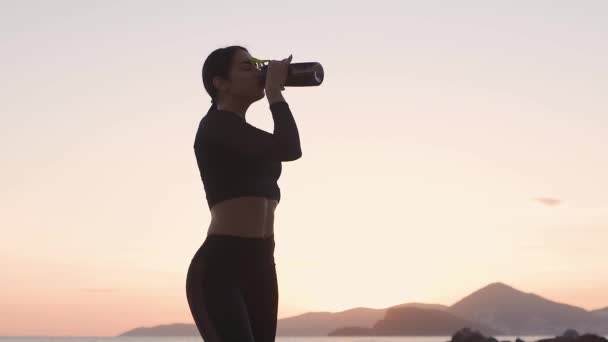 Sportif seksi kadın gün batımında sahilde su içiyor. — Stok video