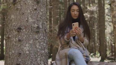 Ormanda telefon kullanan güzel bir kadın ahşap kütüğün üzerinde oturuyor.