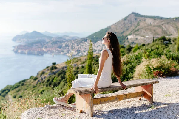 Hermosa chica en vestido de verano relajarse con vistas al mar y las montañas —  Fotos de Stock