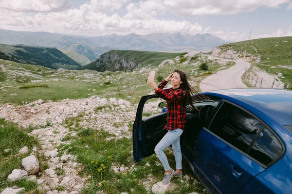 魅力的な女性は車で山の中でスマートフォンを使い — ストック写真