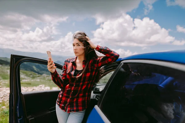 Wanita yang menarik bepergian dengan mobil dan menggunakan smartphone di pegunungan — Stok Foto