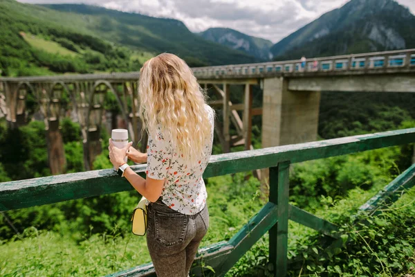 Γυναίκα ταξιδιώτη κρατώντας κούπα καφέ με θέα στα βουνά — Φωτογραφία Αρχείου