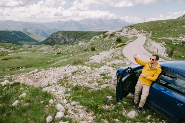 Pria tampan bepergian dengan mobil dan menggunakan smartphone di pegunungan — Stok Foto