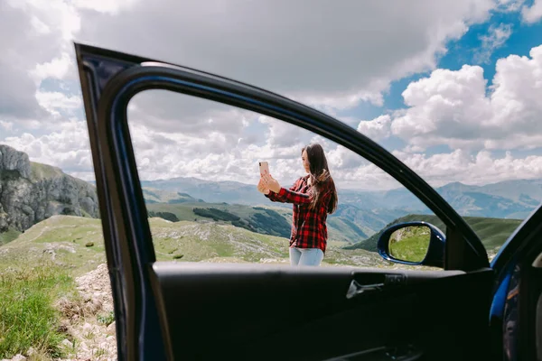 Mooie vrouw toerist met smartphone in de bergen en reizen met de auto — Stockfoto