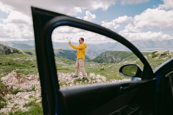 Pria perjalanan dengan mobil dan menggunakan smartphone pada liburan di pegunungan — Stok Foto