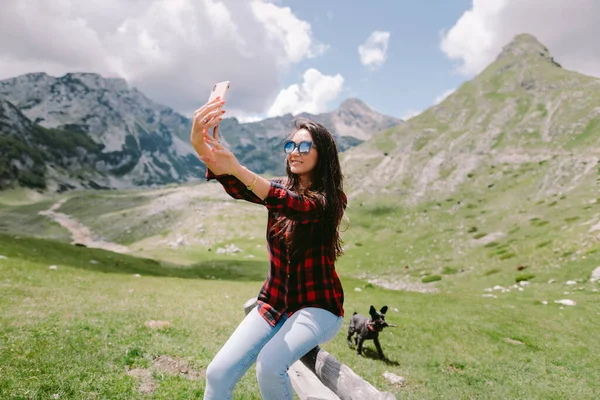 Wanita bahagia bepergian dengan anjing dan menggunakan smartphone di pedesaan — Stok Foto