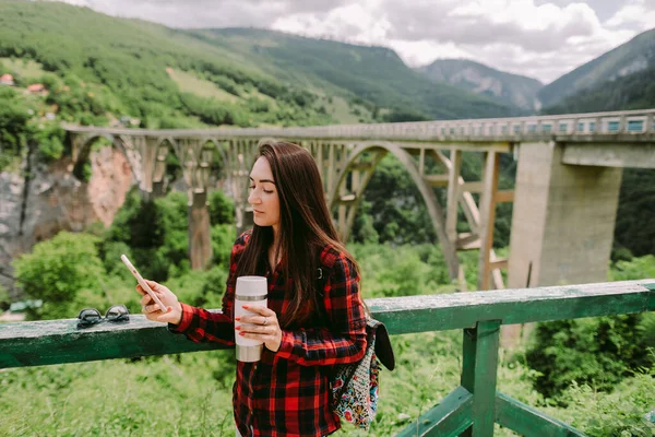 นักท่องเที่ยวผู้หญิงใช้สมาร์ทโฟนและดื่มกาแฟในชนบท — ภาพถ่ายสต็อก