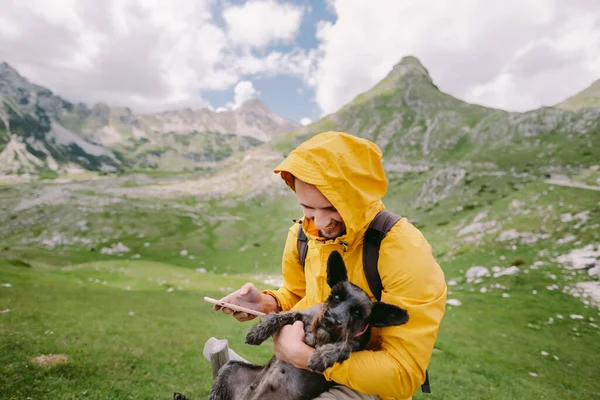 ผู้ชายเดินทางกับสุนัขโดยใช้สมาร์ทโฟนในชนบทพร้อมวิวภูเขา — ภาพถ่ายสต็อก