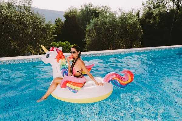 Wanita bersantai di kolam renang pada inflatable pool mainan unicorn dan makan semangka — Stok Foto