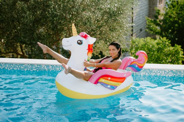 Wanita atraktif bersantai di kolam renang di karet pantai floaty mainan unicorn di kolam renang — Stok Foto
