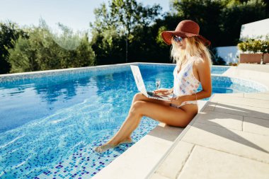Uzaktan çalışan ve yüzme havuzunda dizüstü bilgisayar kullanan bir kadın.