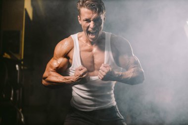 Vücut geliştiren adam kaslarını şişiriyor ve yırtık gömlekle poz veriyor.