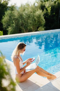 Laptop kullanan ve havuz kenarında çalışan bir kadın.