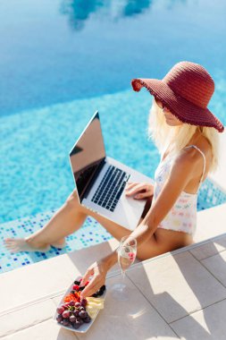 Laptop kullanan ve havuz kenarında çalışan bir kadın.