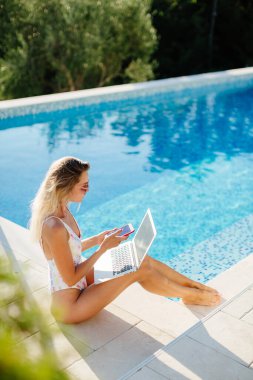 Laptop kullanan ve havuz kenarında çalışan bir kadın.