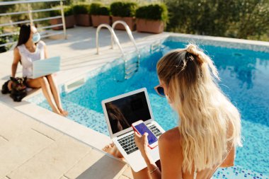 Sosyal mesafede dizüstü bilgisayar kullanan kadınlar yüz maskesi takıyor.