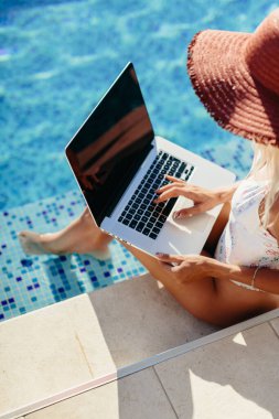 Laptop kullanan ve havuz kenarında çalışan bir kadın.